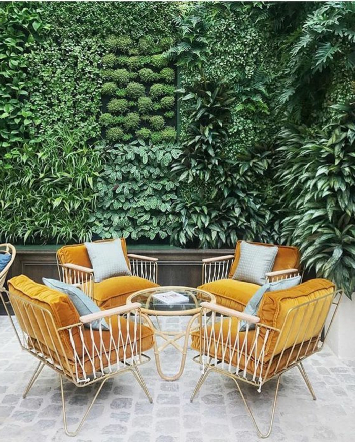 aménagement extérieur maison, décoration murale extérieure, mur vert qui combine plusieurs types de plantes, salon de jardin avec quatre fauteuils aux cadres métalliques blancs avec des coussins en velours orange, petite table ronde avec plan en verre