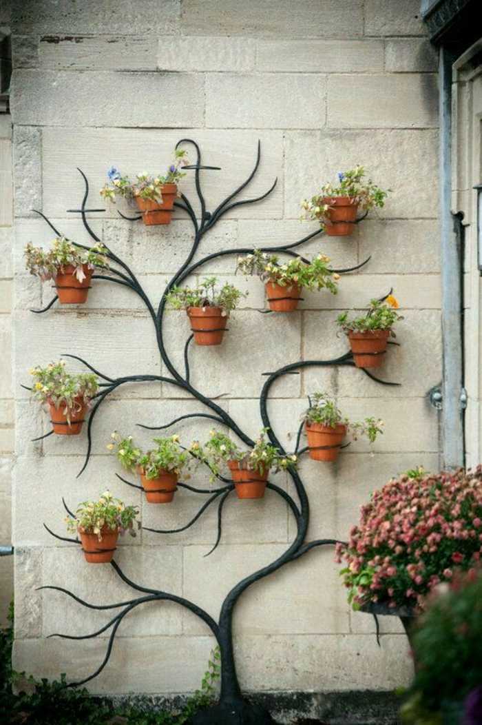 aménagement extérieur maison, mur orné de porte-plante en métal noir en forme d'arbre, avec des branches sur lesquelles on a suspendu des pots avec des fleurs