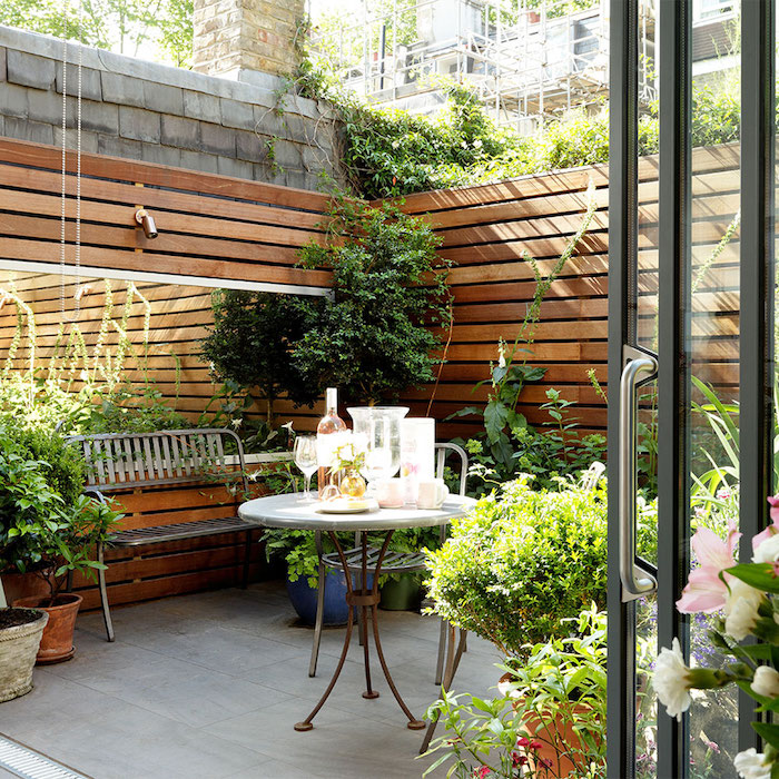 comment amenager un cour exterieur en terrasse moderne avec banc, chaise et table metallique, grand miroir, séparation en bois, plantes vertes en pots