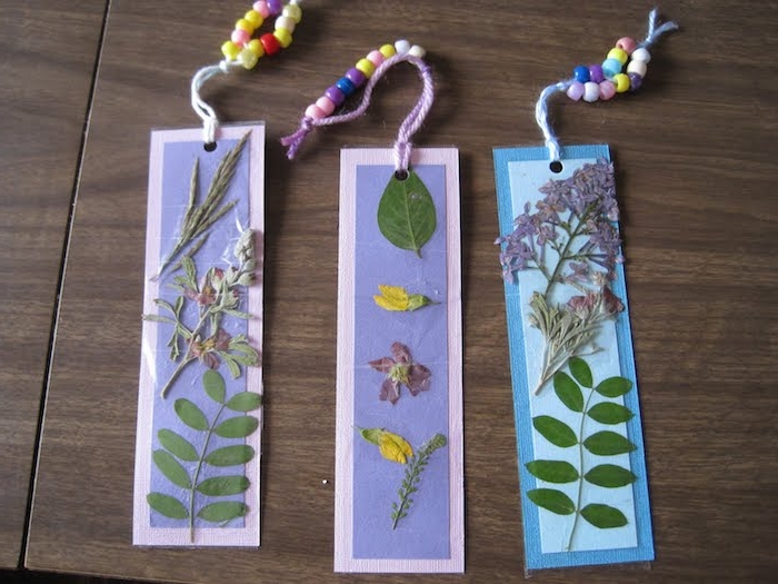 marque page herbier sur un papier couvert de feutrine, fleurs et feuilles collées dessus, un bracelet attaché