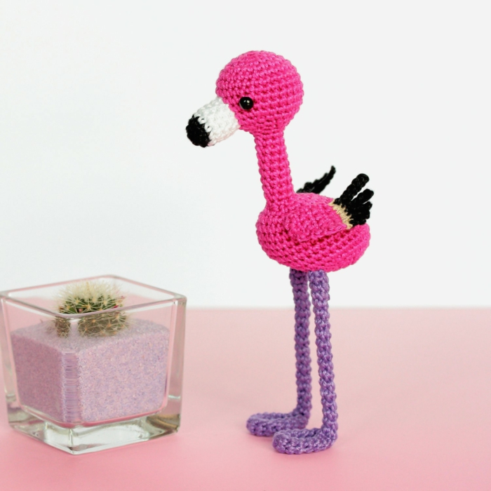 petit jouet pour enfants tricoté en forme de flamant, déco flamant rose, figure posée près d'un pot en verre avec du sable et un cactus