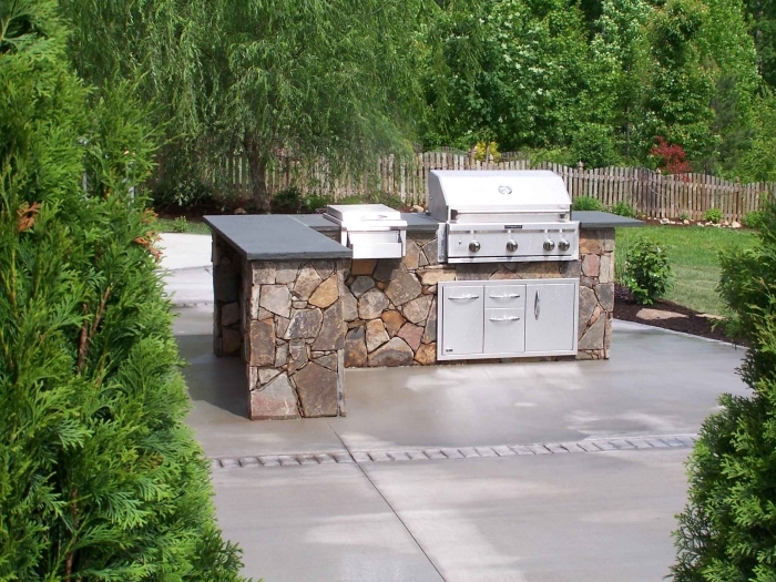 exemple de cuisine ouverte dans le jardin avec ilot en pierre et équipement barbecue et armoires à portes inox