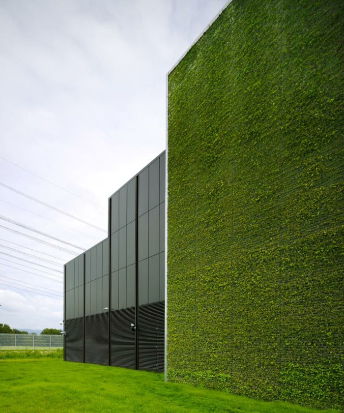 bâtiment industriel avec un mur vegetal exterieur, une partie de l'édifice est en métal noir et de fenêtres noires, grand champ vert