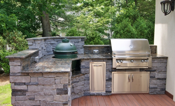 modele de cuisine aménagée sur une terrasse au parquet de bois marron avec ilot en pierres et barbecue en inox