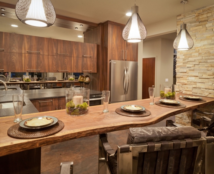 déco de cuisine avec ilot central en bois brut et meubles haut en bois foncé, modèle de cuisine au plafond blanc et mur en pierre