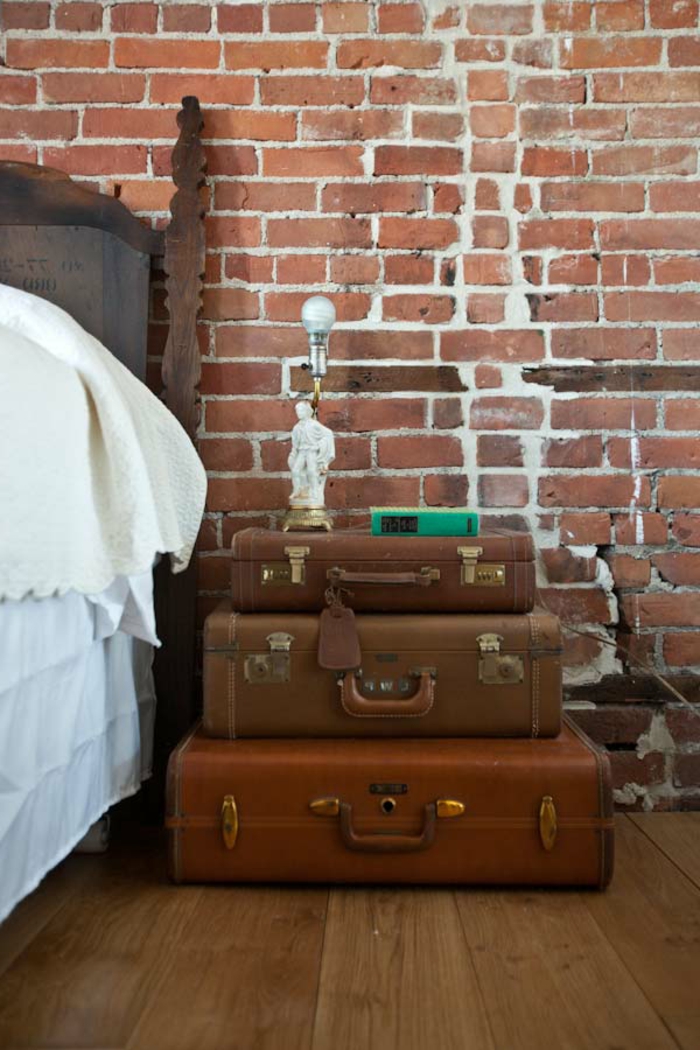 trois valises vintage empilés comme table de chevet originale, murs en briques, chambre vintage industrielle 
