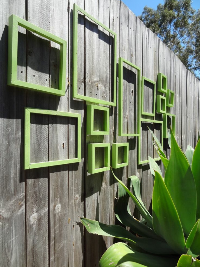 habillage mur exterieur avec des vieux cadres de tableaux repeints en vert réséda, clôture de jardin en bois gris avec effet vieilli, grande plante verte exotique