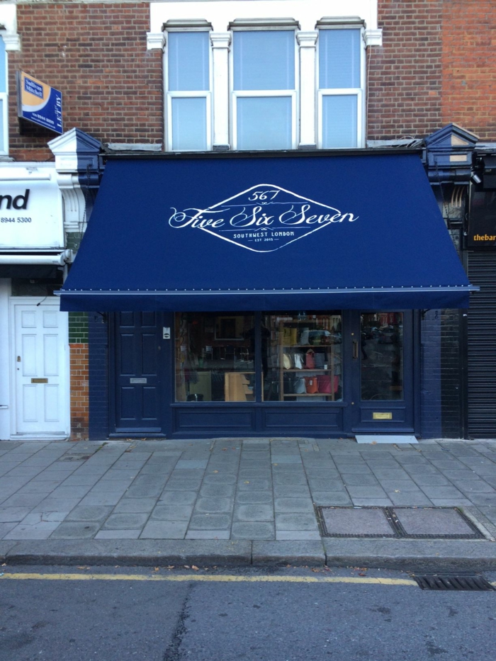 un store banne motorisé en bleu royal avec logo et inscriptions de publicités en blanc, magasin avec portes et cadres fenêtres peintes en bleu roi