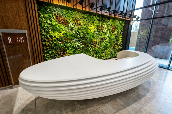 mur végétal intérieur, hôtel, réception avec grand meuble ovale blanc au design futuriste, mur végétalisé illuminé par des spots luminaires en métal noir