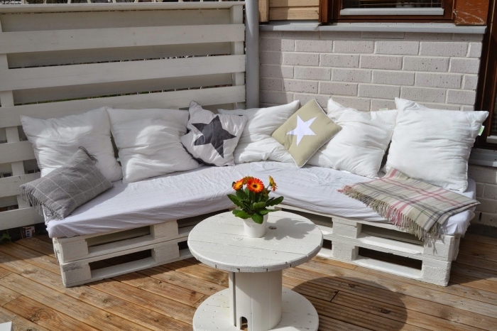 coin extérieur au plancher de bois aménagé avec meuble d'angle DIY en palettes de bois couvert de coussins avec petite table