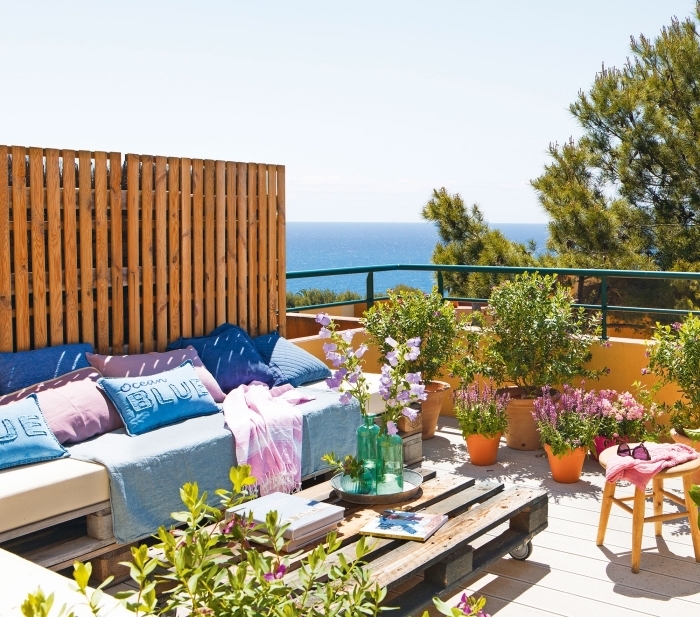 exemple de salon de jardin en palette DIY avec un canapé couvert de coussins bleu rose et une table basse