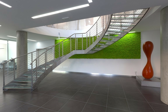 mur végétal intérieur, édifice public avec escaliers en demi-tournant en métal clair aluminium, sol recouvert de dalles de carrelage couleur taupe, oeuvre artistique abstraite, figure en rouge