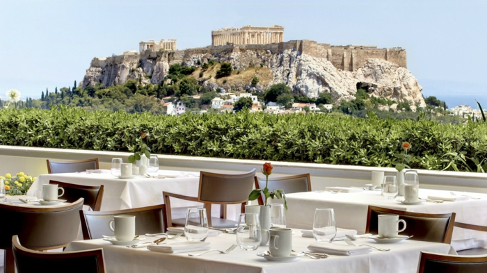 un mur végétalisé comme garde-corps dans un restaurant d'Athènes, chaises en marron clair, belle vue sur l'Acropole, ciel bleu sans nuages 