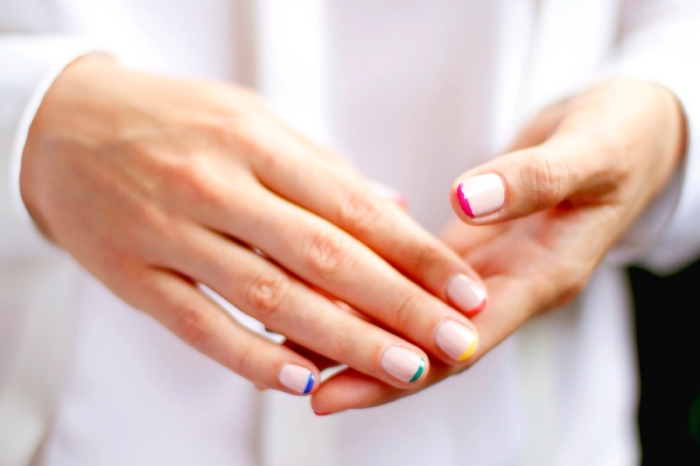 vernis-de-base-nude-manucure-french-multicolore-soins-mains-ongle-rose-pale-manucure-ongles-courts-technique-décoration-nail-art manucure moderne avec vernis de base nude et traits sur les bouts en différentes couleurs, idée pour faire une déco nail art