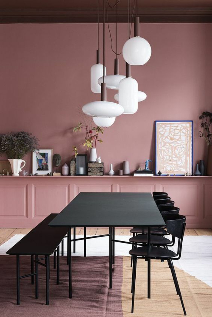 murs en vieux rose, rose noir et blanc, sept grands luminaires en verre blanc mat au-dessus d'une table rectangulaire noire, cinq chaises en métal et bois noir
