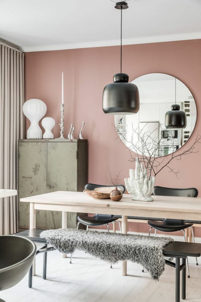 murs en couleur rose pale, luminaire en céramique noire suspendu sur un fil noir, grand miroir rond, table rectangulaire en bois clair