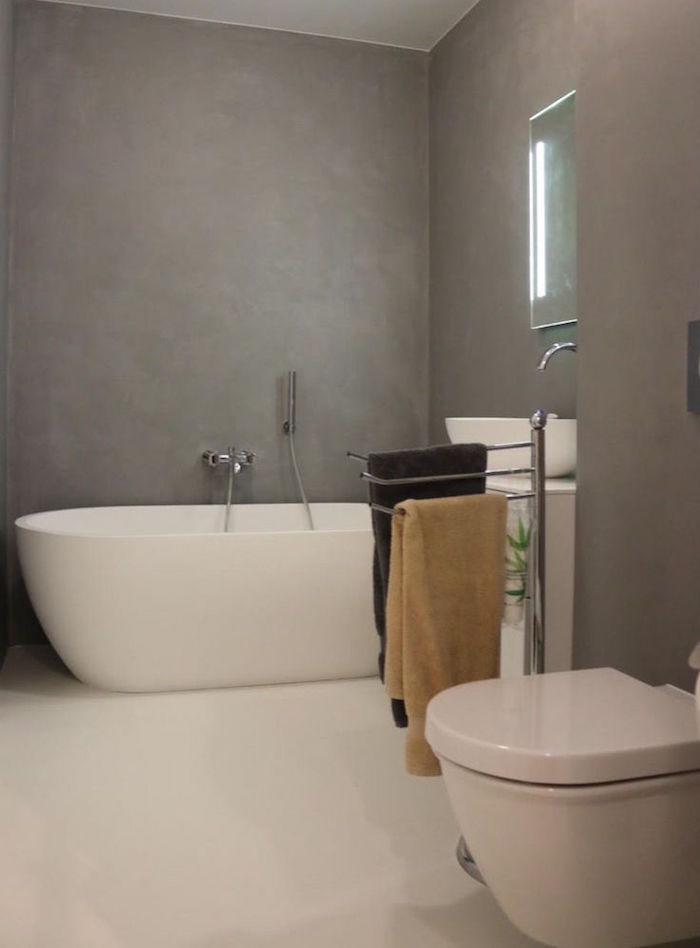 sdb rénovée style moderne avec mur en gris béton ciré sol carrelage blanc et baignoire ilot ovale