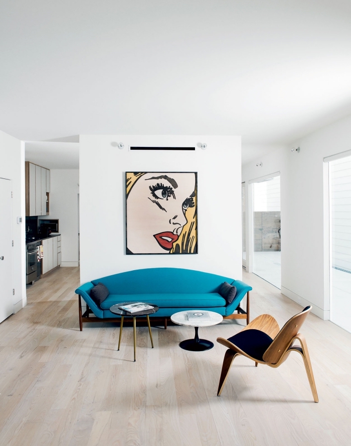associé avec un tableau pop art original et sublimé par de petites tâches de noir, le canapé bleu canard se fait élément central dans ce salon blanc immaculé