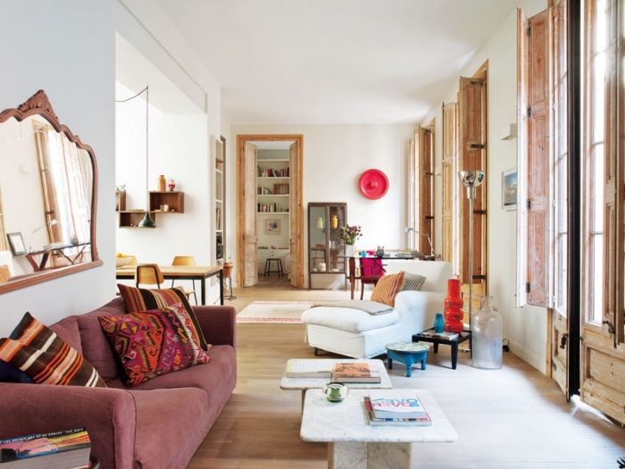 intérieur chaleureux dans un salon blanc avec fenêtres de bois et parquet clair, modèle de canapé rose couvert de coussins ethniques
