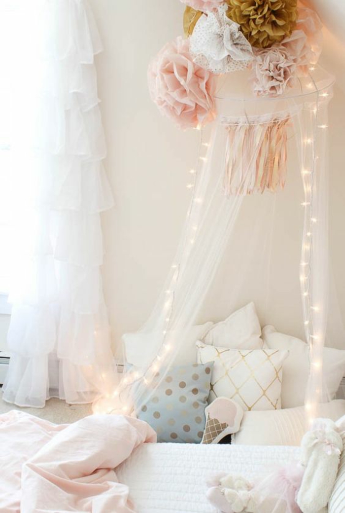 chambre d'enfant, fillette romantique, gros pompons en marron, rose et blanc au-dessus du moustiquaire blanc fin sur le lit, guirlande a pile, rideaux a volants blancs