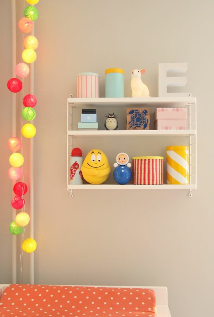 guirlande lumineuse boule coton multicolore, chambre de bébé, meuble pour changer les couches, étagères blanches avec des boites de rangement rondes et carrées en couleurs pastels