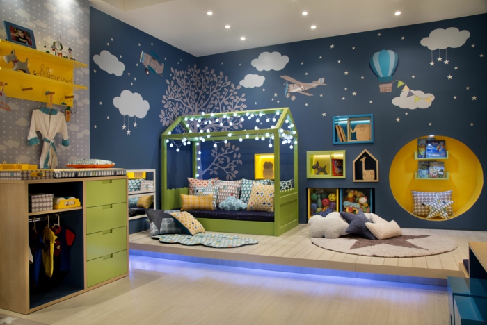 meuble montessori, lit cabane montessori en bois peint en vert, murs peints en bleu canard, avec des motifs nuages blancs et montgolfières colorées en bleu pastel et blanc