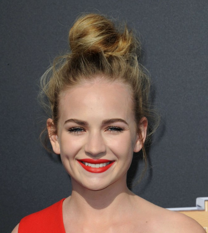 chignon-facile-à-faire-chignon-haut-robe-rouge-asymétrique-rouge-à-lèvres-écarlate chignon haut, cheveux blonds, lèvres rouges, maquillage des yeux naturel