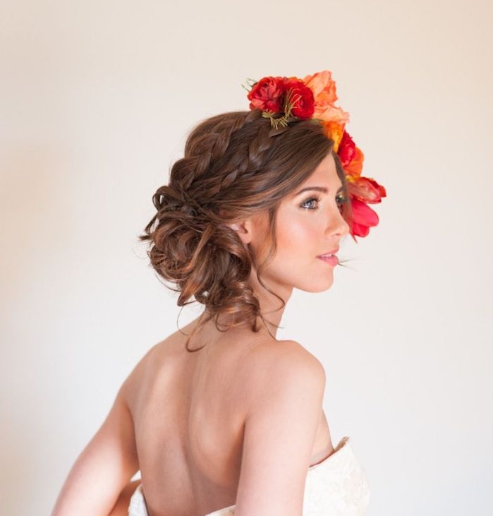 coiffure-tresse-mariage-avec-deux-tresses-et-boucles-en-chignon-bohème-bas-et-des-fleurs-sur-le-côté-robe-de-mariée-blanche coiffure tresse africaine sur cheveux longs bouclés couleur chatain, bouquet de fleurs rouges du côté de la tête
