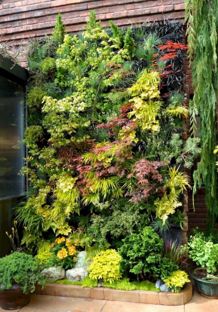 un coin de verdure rassérénante aménagé dans le jardin avec un mur végétal composé de plantes de couleur et de taille variée