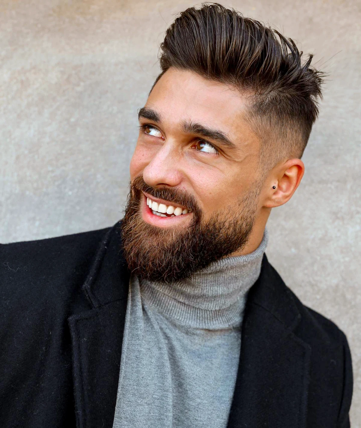 coupe de cheveux homme court avec du volume et barbe homme pull gris veste noire