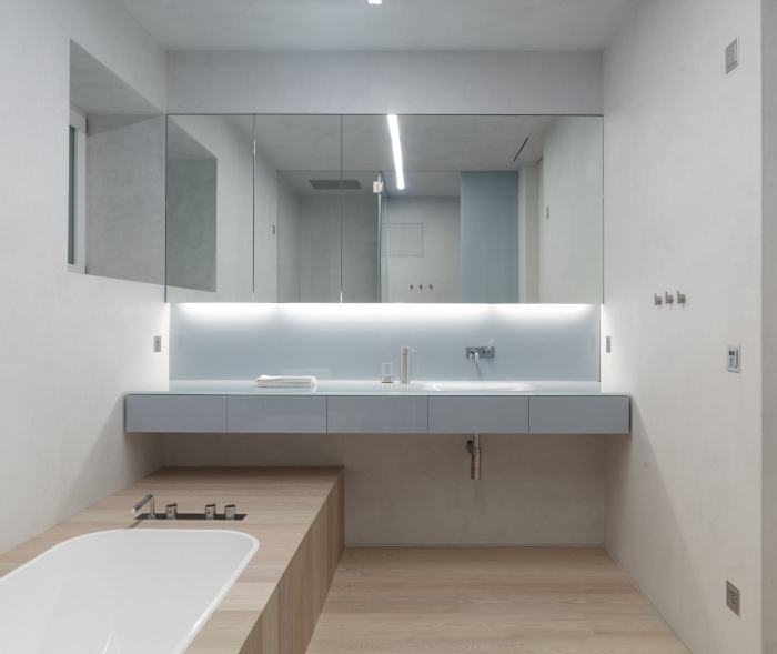 petite salle de bain avec baignoire et revêtement de sol à design bois aux murs blancs avec large miroir et éclairage sous meuble