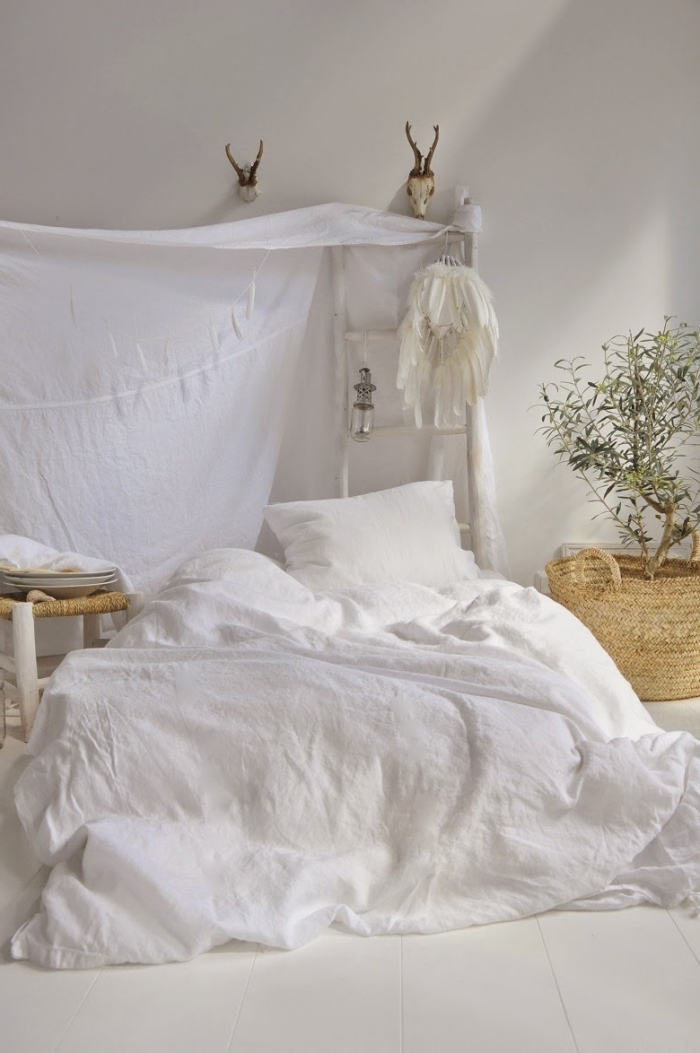 décoration de lit au sol à imitation lit baldaquin avec un drap blanc et échelle de bois peint blanc avec attrape rêve en plumes blanches