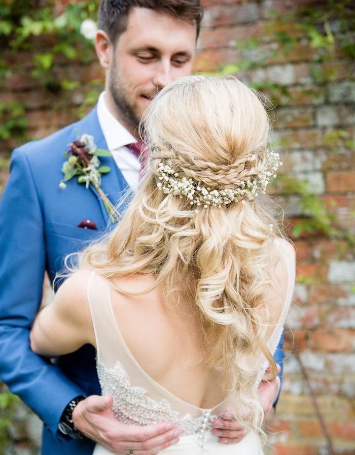 deux-petites-tresses-en-couronne-derrière-la-tête-couronne-de-fleurs-blanches-et-boucles-blondes-robe-de-mariée-champetre-dos-nu tresses sur les cheveux de côté de la tête sur cheveux longs ondulés et couronne de fleurs blanches