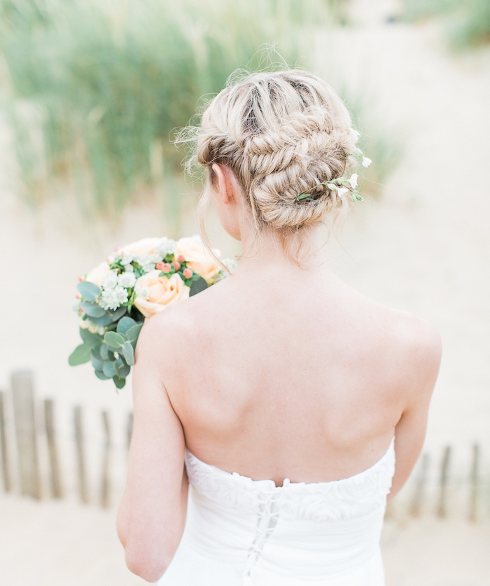 idée de coiffure tresse mariage avec des tresses en épi de blé ramenées en arrière sous la forme de chignon, robe de mariée blanche