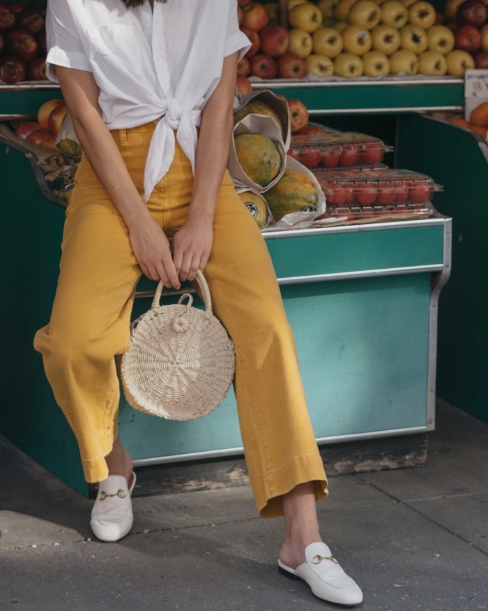 escarpins-blancs-sac-a-main-rond-beige-chemise-blanche-manches-courtes-chemise-nouée-pantalon-fluide-couleur-jaune-tenue-été-femme-mode modèle de pantalon large à taille haute avec chemise blanche nouée et sac à main de style balinais beige