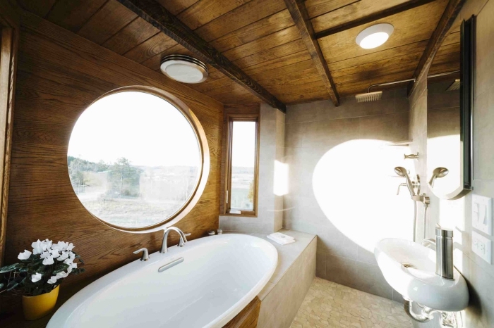 modèle de salle de bain mansardée équipée d'une baignoire ovale au plafond de bois foncé et revêtement en carrelage gris clair