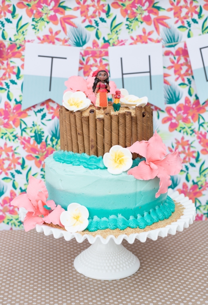 jolie idée de deco vaiana sur un gâteau à deux étages à design océan et sable avec figurines Vaiana et Hei hei