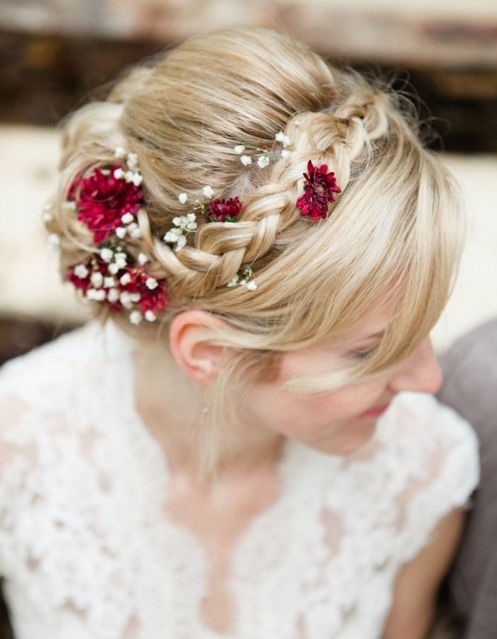 idée-de-tresse-en-couronne-avec-des-mèches-blondes-libres-chignon-et-fleurs-blanches-et-rouges coiffure de mariée avec une tresse en couronne, mèches libres de devant et décoration de fleurs rouges et blanches