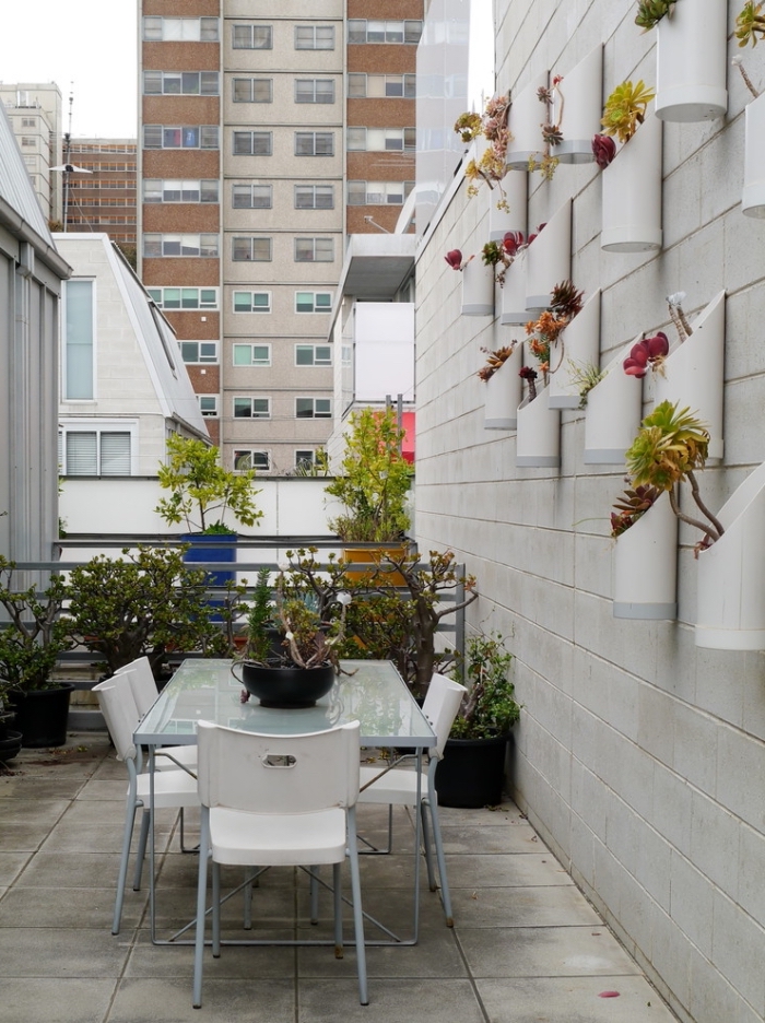 des pots originaux avec des plantes exotiques, fixés au mur qui constituent un mur vegetal exterieur original en joli contraste avec les murs en ciment et le carrelage du balcon