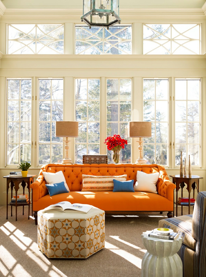 sofa orange capitonné, pouf beige, lampes de tables beiges, grande fenêtre, plafonnier lanterne