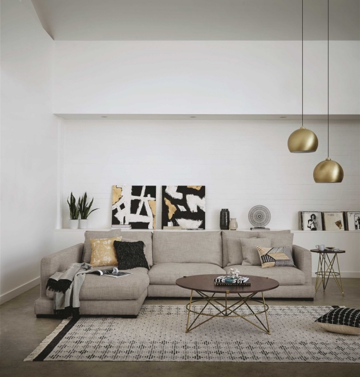 modèle de salon moderne aux murs blancs aménagé avec canapé d'angle et accessoires en finitions or et motifs ethniques