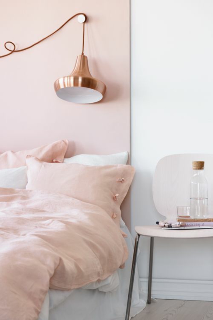 tete de lit en rose poudree, linge de lit couverture et coussins en couleur rose pale, luminaire en couleur or rose, chaise en plastique blanche avec des pieds en métal clair