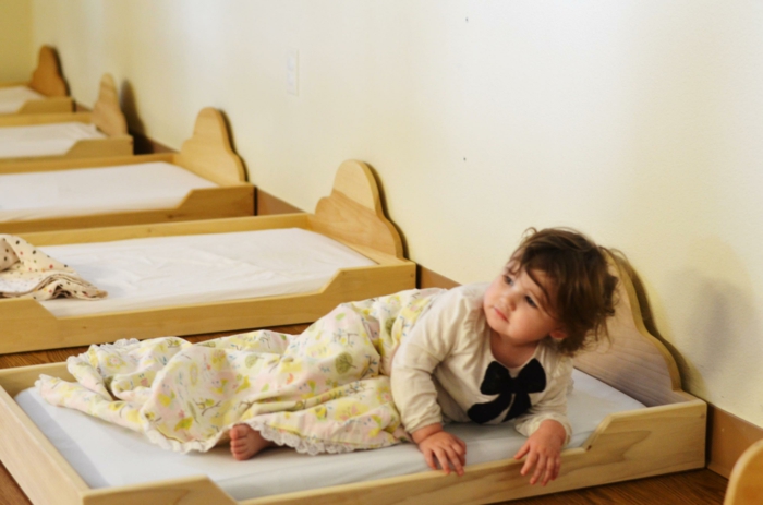 lit cabane montessori, meuble montessori, chambre montessori, six lits en bois clair dans une garderie d'enfants, enfant de quatre ans qui se lève de son lit 