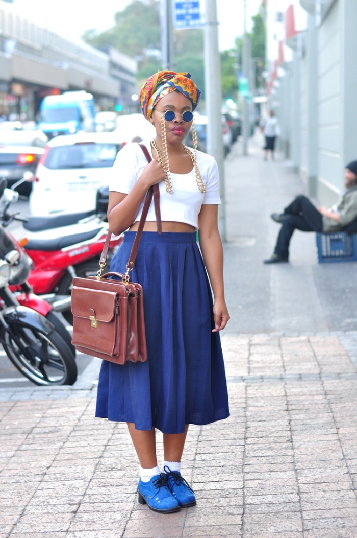 la mode africaine moderne, look vintage et chic en jupe midi bleu et crop top blanc, accessoirisés avec un attachée de foulard wax et un sac cartable en cuir marron