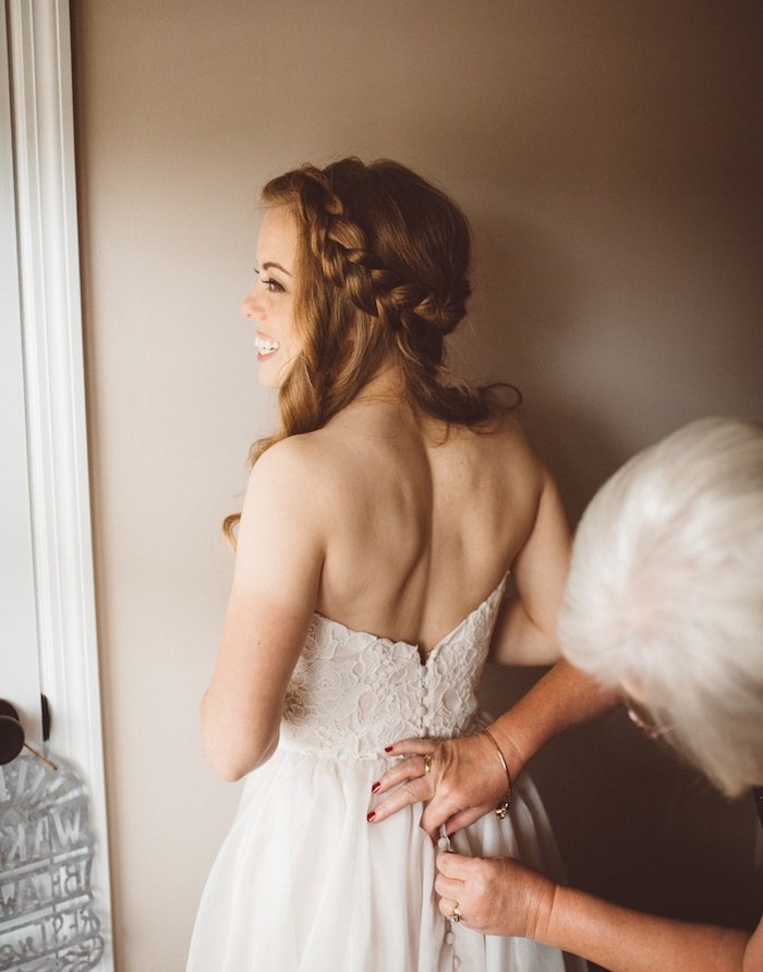 modele-de-tresse-couronne-autour-de-la-tete-et-des-cheveux-longs-ondulés-robe-de-mariée-avec-bustier tresse sur le coté de cheveux roux, femme cheveux ondulés, robe avec un top en dentelle, jupe en tulle