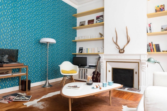 un mur bleu canard dans un salon blanc et bois d'ambiance scandinave, papier peint imprimé vintage en bleu vert saturé qui s'harmonise avec l'intérieur blanc et le bois blond