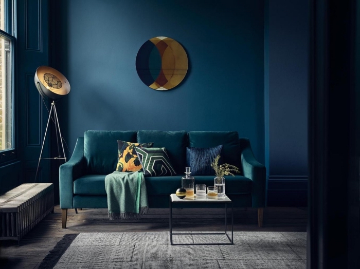 salon élégant et sophistiqué où la couleur bleu canard sur les murs et sur le canapé est mise en valeur par les accents déco lumineux