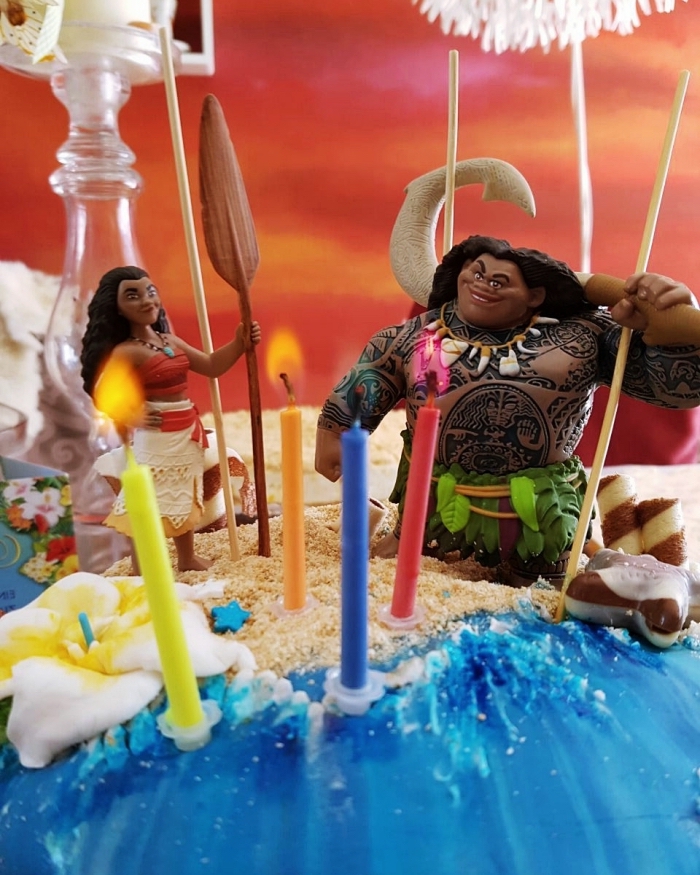 idée de décoration de gâteau sur le thème de Disney avec figurines des personnages Vaiana et Maui sur une couche de sable en biscuits émiettés