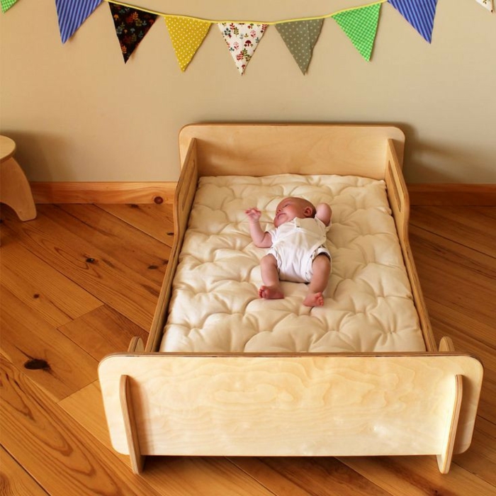 chambre montessori, meuble lit montessori, décoration murale en couleurs au-dessus du lit, ambiance tranquille, bébé heureux dans son lit