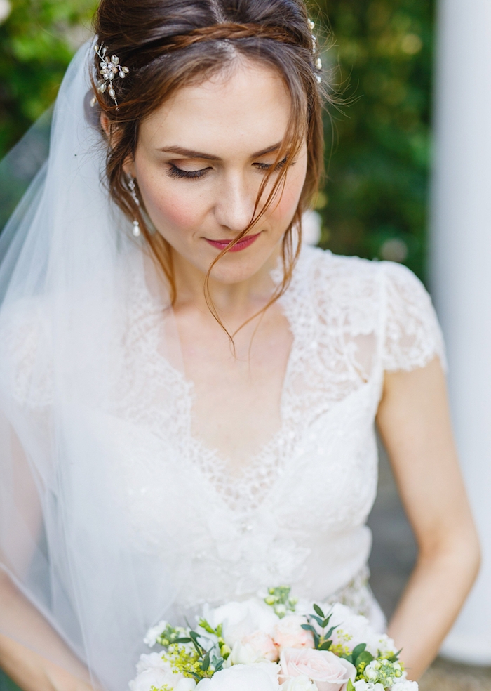 modele-de-coiffure-chignon-tresse-petite-trsse-en-couronne-mèches-libres-robe-de-mariée-manches-courtes-dentelle petites tresse en serre tete sur cheveux ramenés en arrière en chignon, mèches encadrant le visage